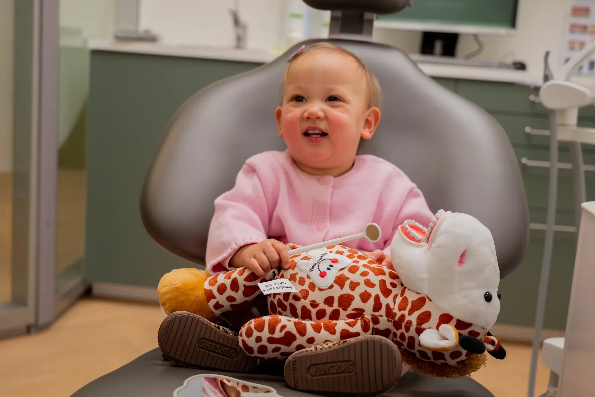 Lachende peuter met knuffelgiraf in de behandelstoel